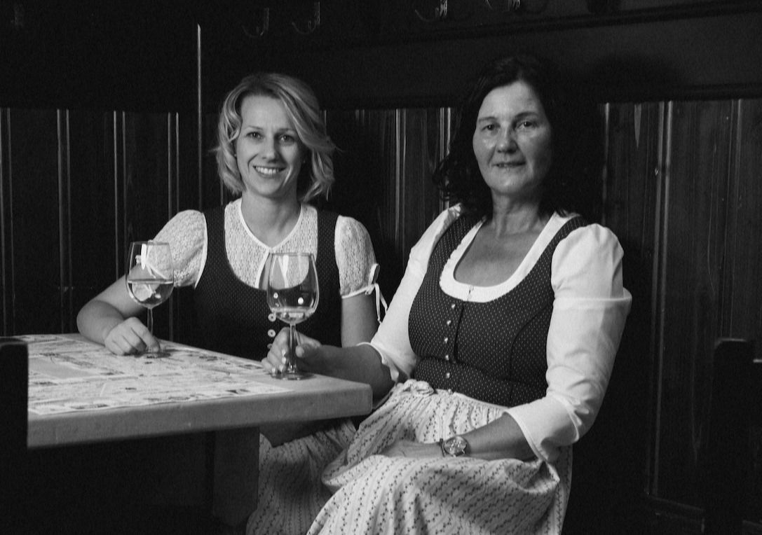 Zwei Frauen in Tracht sitzen an einem Tisch mit einem Glas Wein